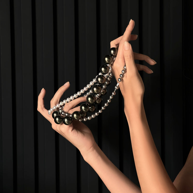 Veilari model hands holding a necklace against a black background